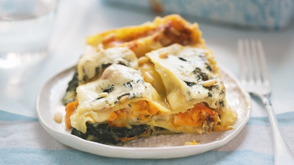 Ein Teller mit einer Portion Kürbis-Lasagne mit Spinat auf einem hellen Tisch.