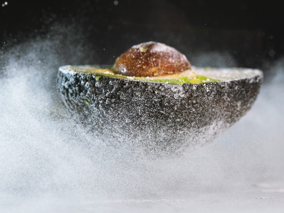 Eine gefrorene Avocadohälfte auf einer Eisfläche nah und von der Seite fotografiert.