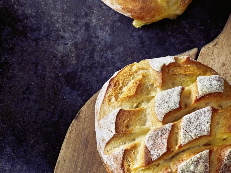 Ein Camembert Brot auf einem Holzbrett und dunkelblauem Tisch von oben fotografiert.