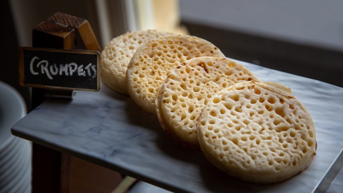 Draufsicht, schräg: 4 ofenfrische Crumpets auf einen dunklen Platte.