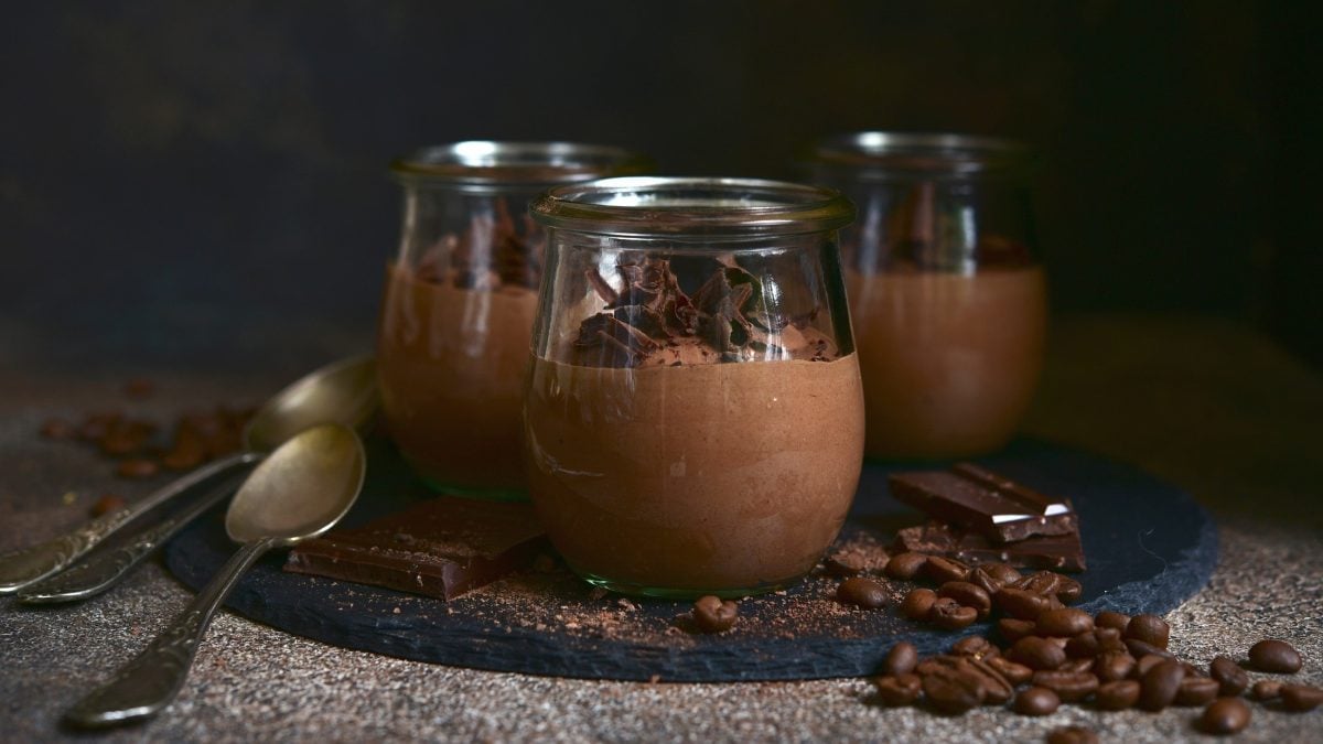Frontal: Drei Gläser Mousse au Café auf einem Untergrund aus Holz vor einem sehr dunklen Hintergrund.