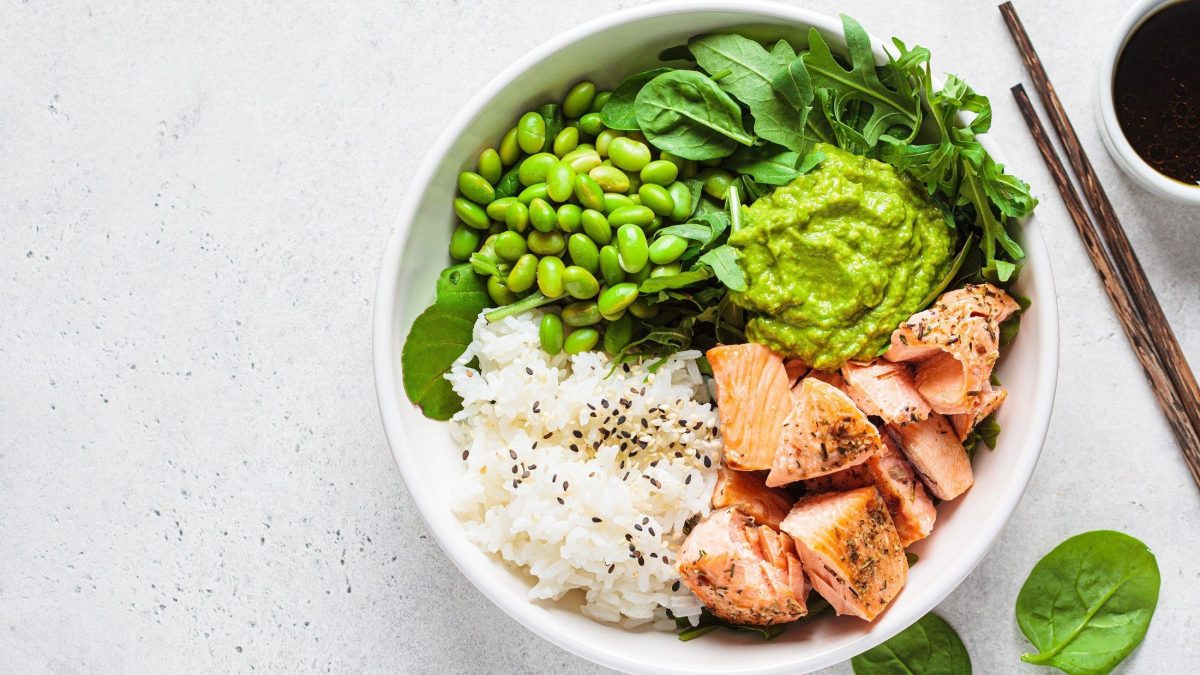 Draufsicht: Heller Untergrund, einen Edamame-Bowl mit Lachs und Esstäbchen.