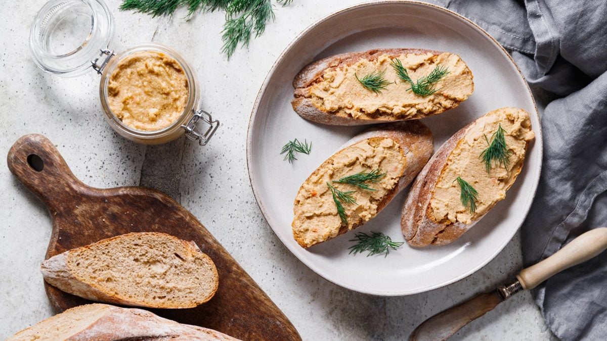 Drei Baguettescheiben mit der Feta-Walnusscreme auf einem weißen Teller und hellem Tisch direkt von oben fotografiert.