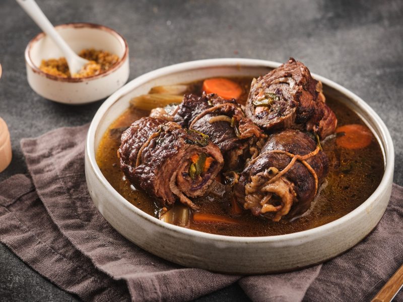 Drei Rouladen in einer weißen Schüssel mit Bratensauce von vorne fotografiert.