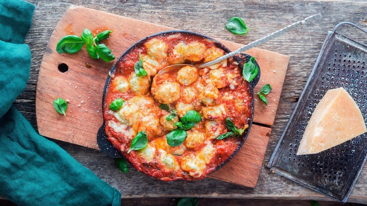 Draufsicht: ein Gnocchi-Auflauf Caprese auf einem Holzbrett.
