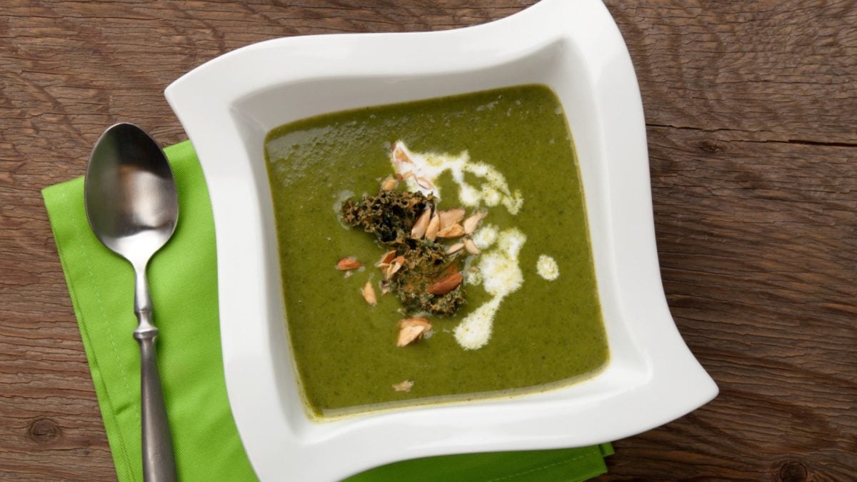 Pürierte Grünkohlsuppe mit Kartoffeln mit Topping auf Holztisch.