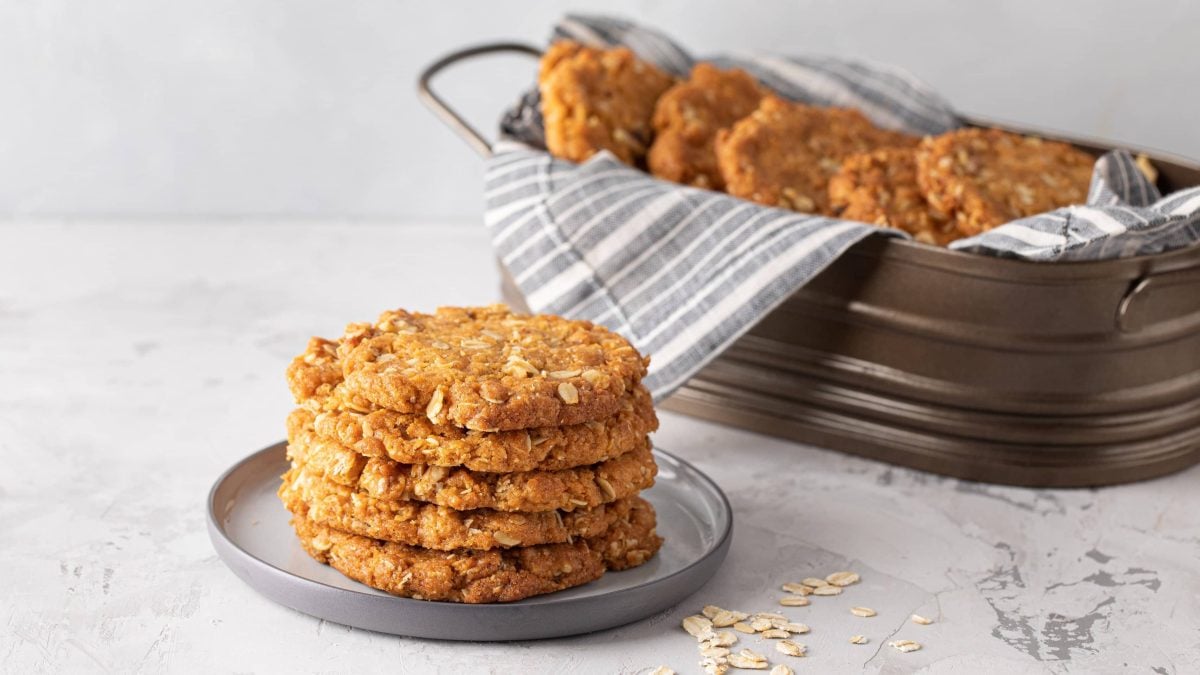 Die Haferflocken-Kokos-Cookies gestapelt auf einem grauen Teller. Im Hintergrund noch mehr Kekse in einer länglichen Backform. Alles von der Seite fotografiert.