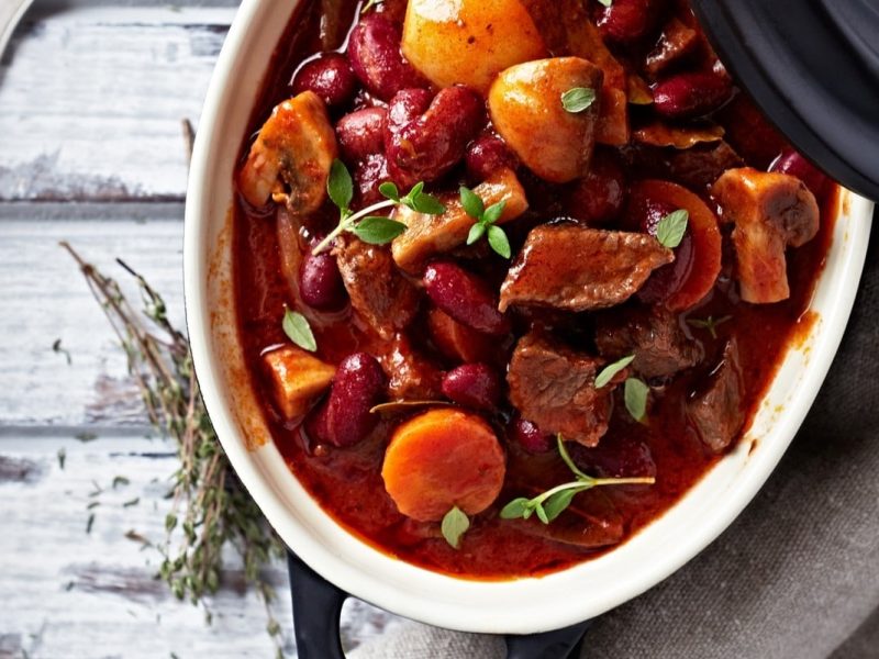 Rustikaler Hirtentopfs, reich gefüllt mit Fleisch, Pilzen und Kidenybohnen. Die Zutaten sind in einer herzhaften Sauce gekocht und präsentieren sich einladend in einem Kochtopf.