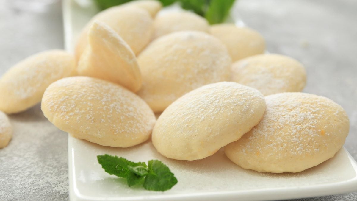 Käsekuchen-Plätzchen mit Puderzucker bestreut auf einem weißen Servierteller.