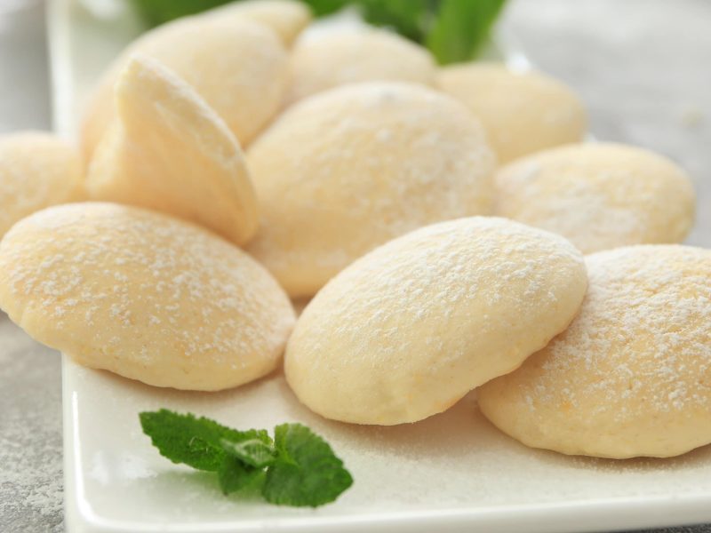 Käsekuchen-Plätzchen mit Puderzucker bestreut auf einem weißen Servierteller.