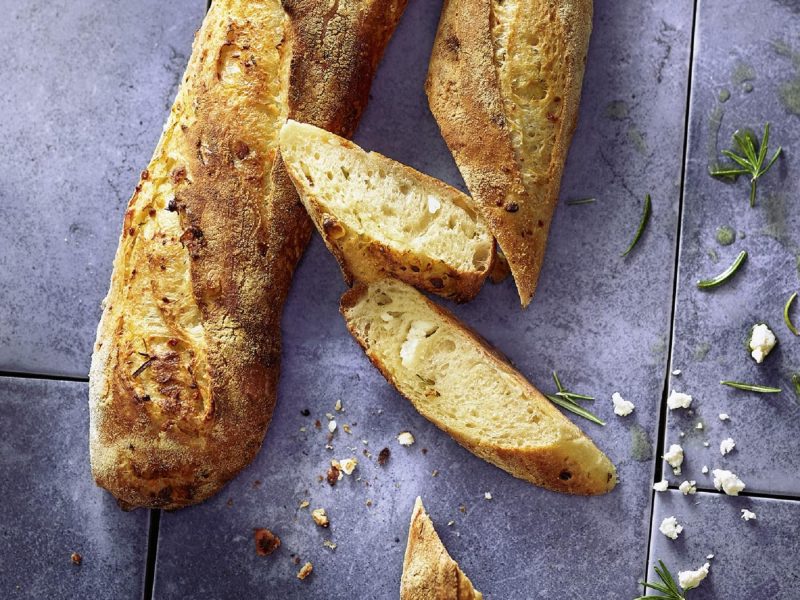 Das Knoblauch-Feta-Baguette auf grauem Untergrund direkt von oben fotografiert.
