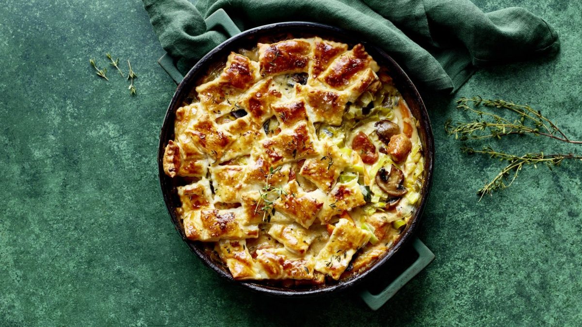 Eine Patchwork-Casserole mit Hähnchen-Lauch-Ragout auf grünem Hintergrund. Oben ein grünes Geschirrtuch. Links und rechts Thymian-Stiele.