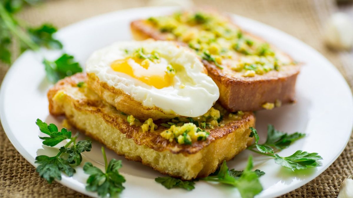 Mehrere Brote mit Kräutern, Knoblauch und Spiegelei. Alles von der Seite fotografiert.