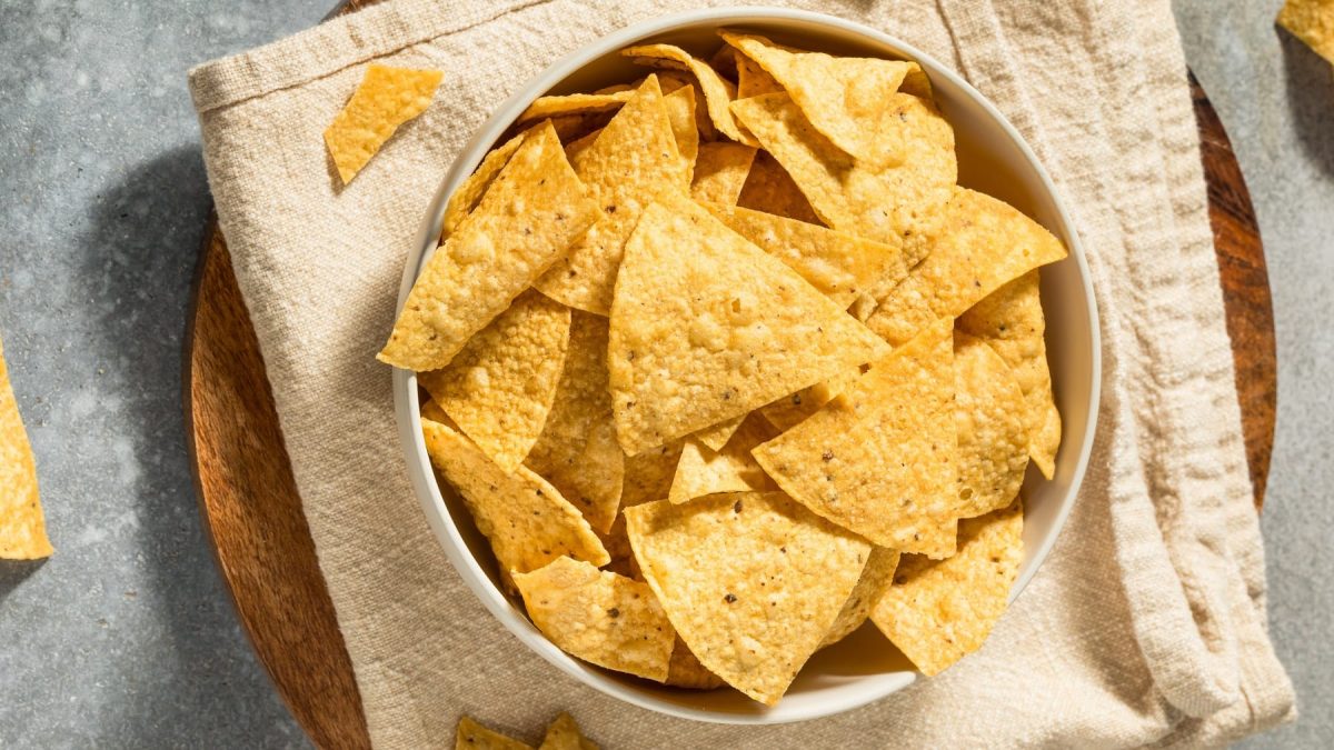 Eine weiße Schale mit den Tortilla Chips auf einer hellen Tischdecke und grauem Tisch. Alles direkt von oben fotografiert.