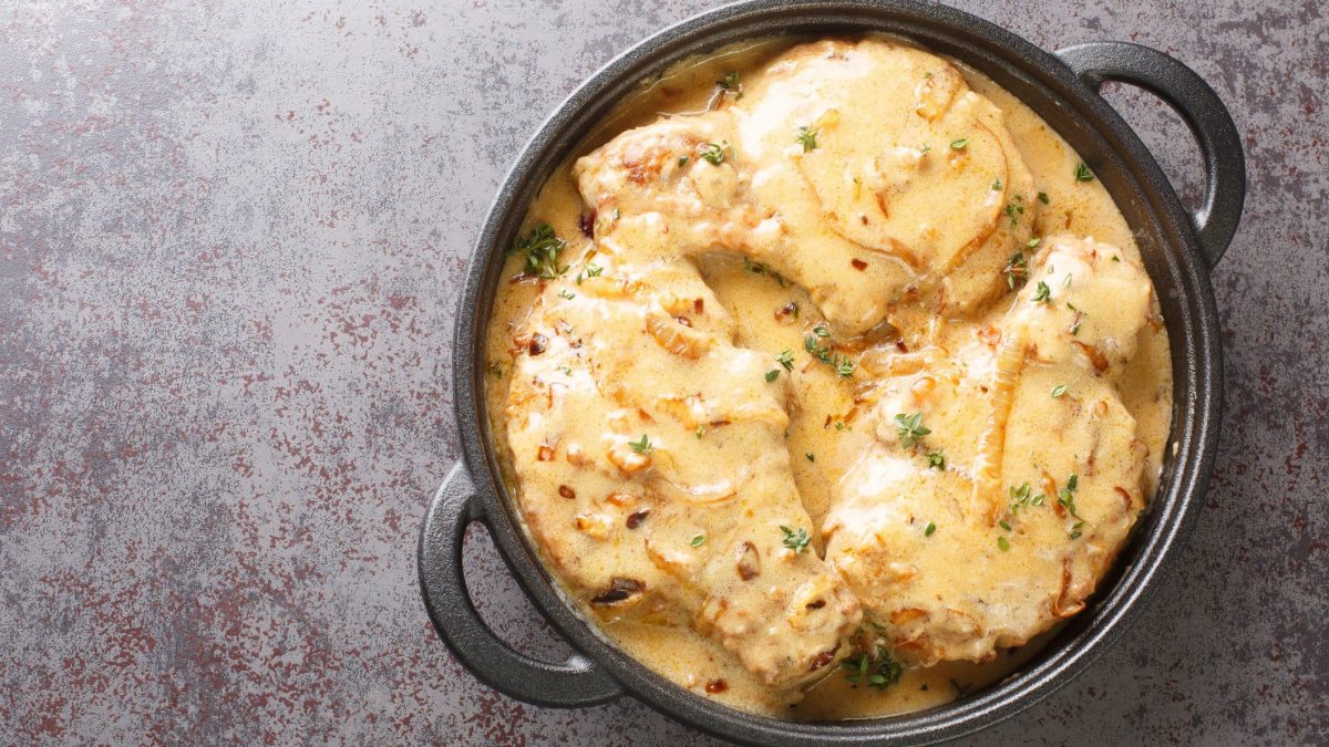 Foto von saftigen Zwiebel-Sahne-Schnitzeln, serviert in einer schwarzen, gusseisernen Pfanne. Die Schnitzel sind reichlich mit einer cremigen Zwiebelsauce bedeckt, die durch ihre glänzende Konsistenz und die sichtbaren Zwiebelstücke auffällt.