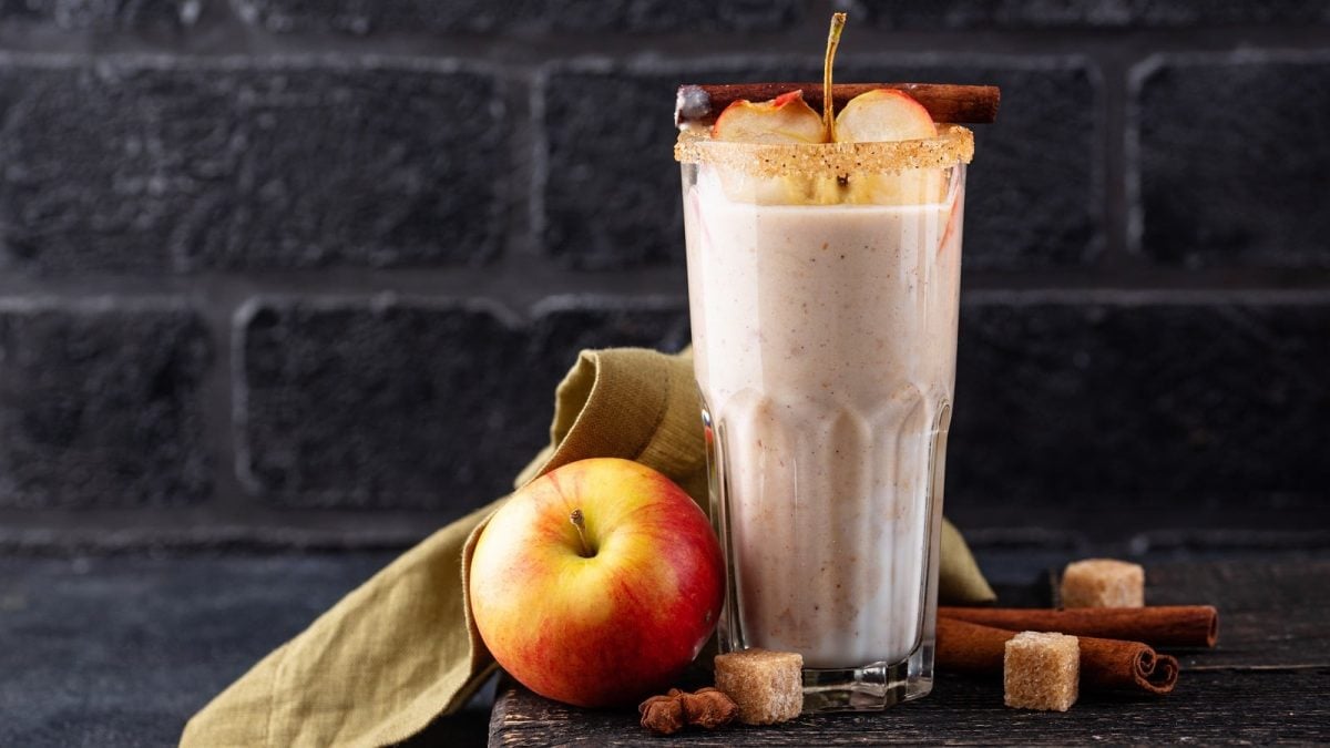 Ein Glas Apple Pie Smoothie vor einer dunkelgrauen Steinwand.