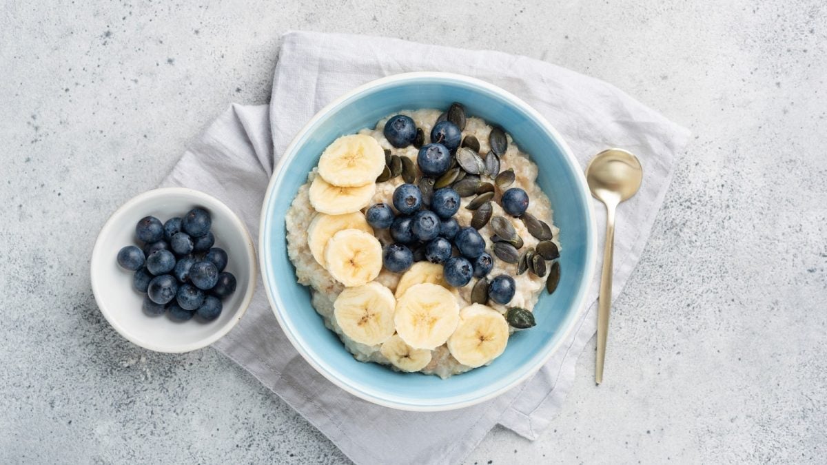 Eine blaue Schüssel Blueberry Cheesecake Porridge auf einem grauen Geschirrtuch.