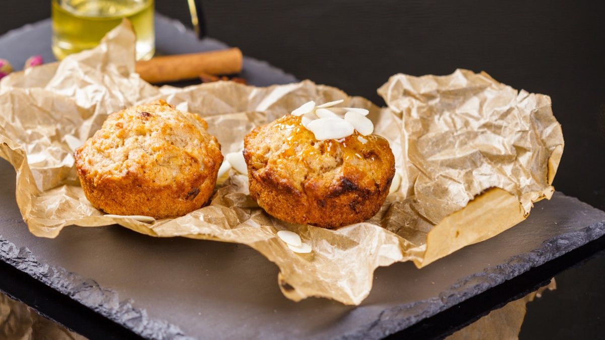 Zwei Apfel-Muffins auf einer schwarzen Schiefertafel mit Backpapier im Hintergrund.