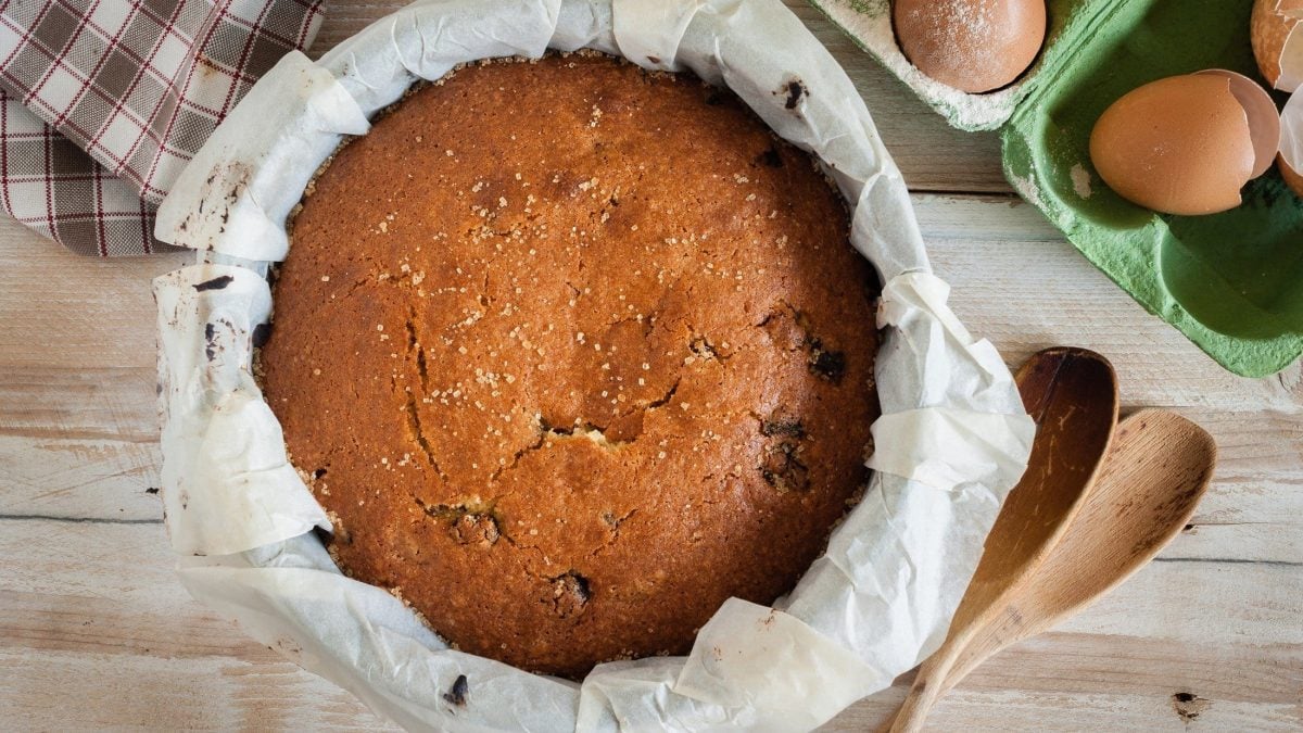 Draufsicht: Auf hellem Holz steht ein britischer Glühwein-Kuchen in einer runden Form. Drum herum liegen Eier und zwei Holzlöffel.