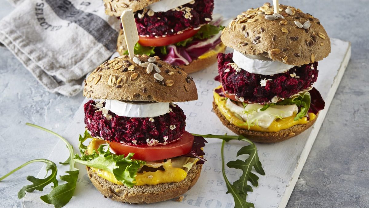 Drei Burger mit roter Bete und Ziegenkäse von vorne fotografiert auf einem grauen Schneidebrett auf einem grauen Hintergrund.