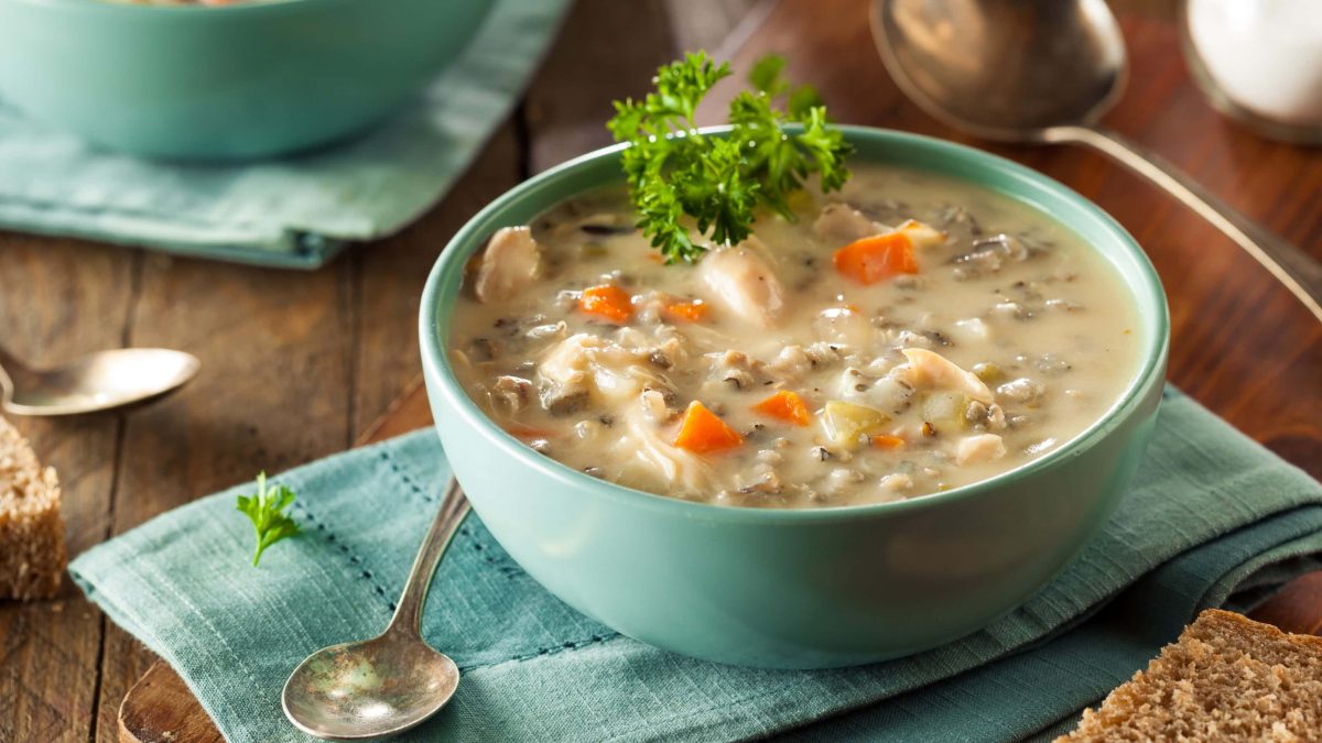 Eine türkisene Schale mit der Hühnersuppe auf einem dunklen Holztisch.