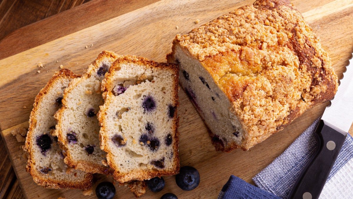 Draufsicht: Ein angeschnittenes Blaubeer-Brot auf einem Holzbrettchen.