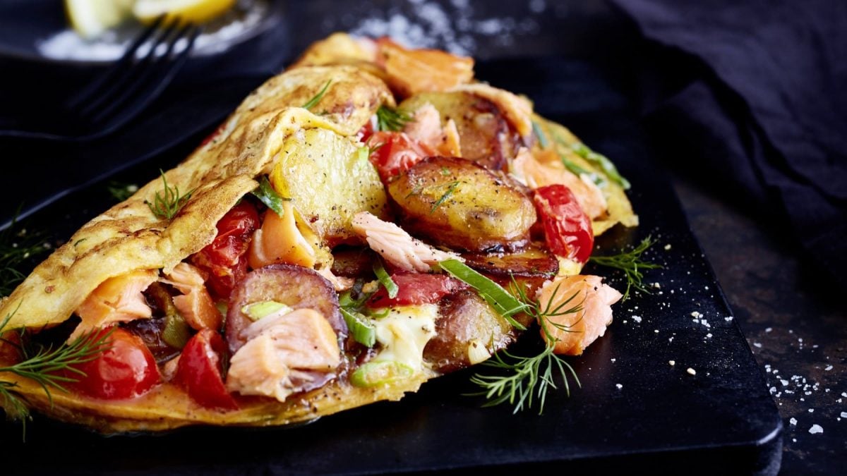 Ein schwarzer Teller mit einer Portion Fischerfrühstück mit Lachs auf einem dunklen Tisch.
