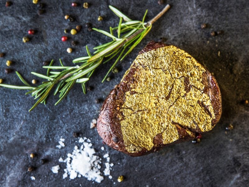 gebratenes Stück Fleisch mit Gold überzogen / frischer Rosmarin und Pfefferkörner / grobes Meersalz