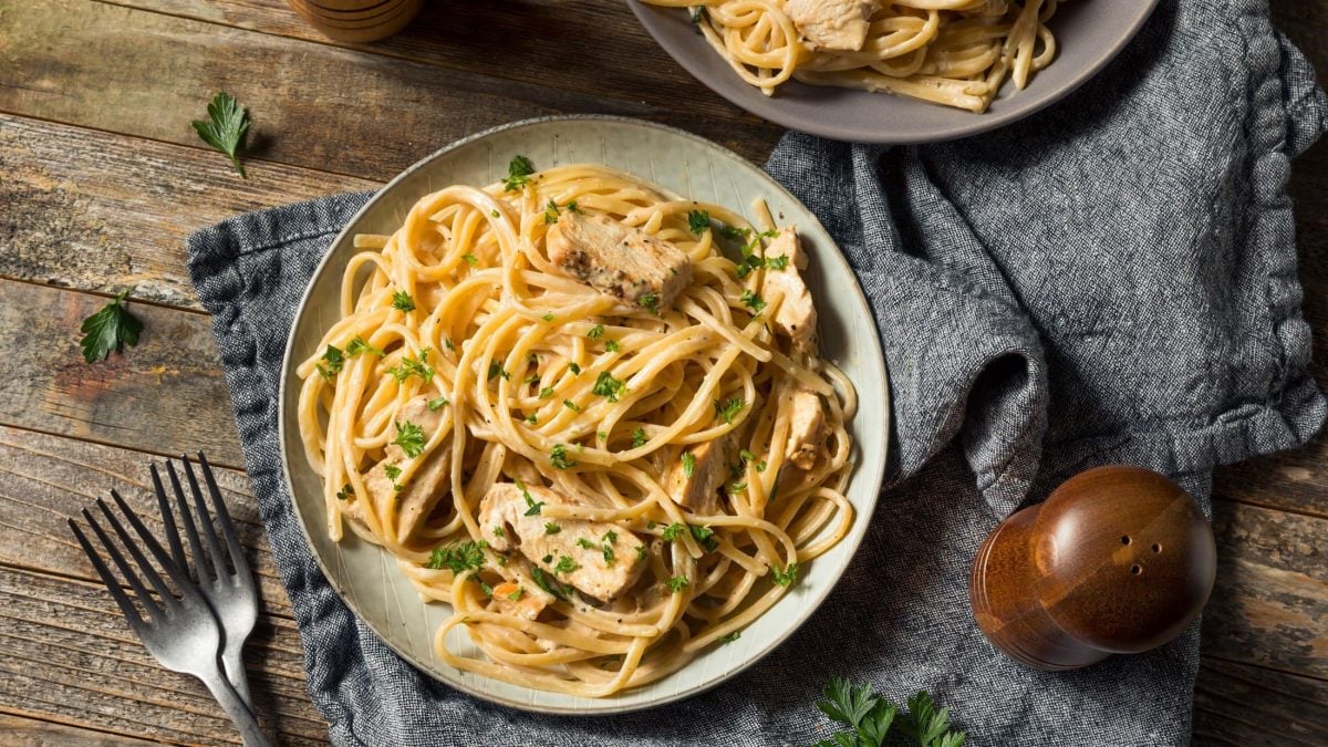 Draufblick: Zwei Teller mit Fettuccine mit Hühnchen auf einem Untergrund aus Holz und einem blauen Tuch. Daneben steht eine Pfeffermühle.