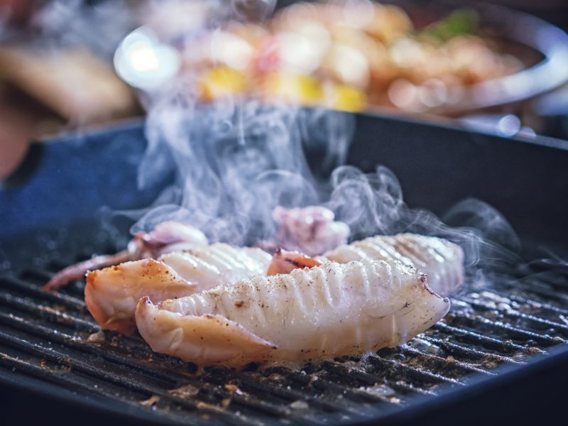Fisch wird in einer Grillpfanne auf einem Gasherd scharf angebraten und dampft.