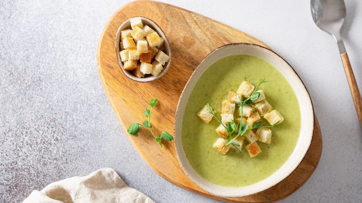Eine weiße Schale mit der Suppe auf einem Holzbrett und weißem Steintisch. Alles direkt von oben fotografiert.