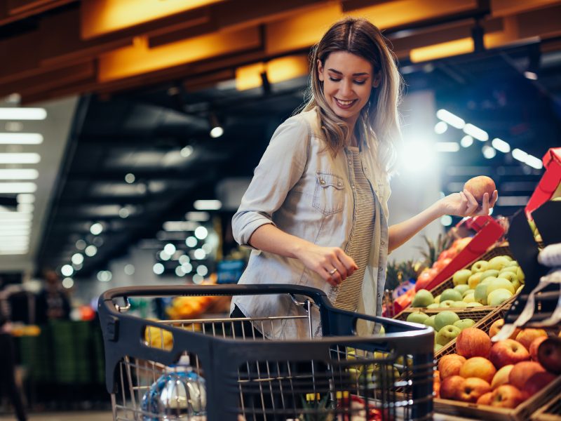 Frau, die einem Supermarkt Obst und Gemüse in ihren Einkaufswagen legt.