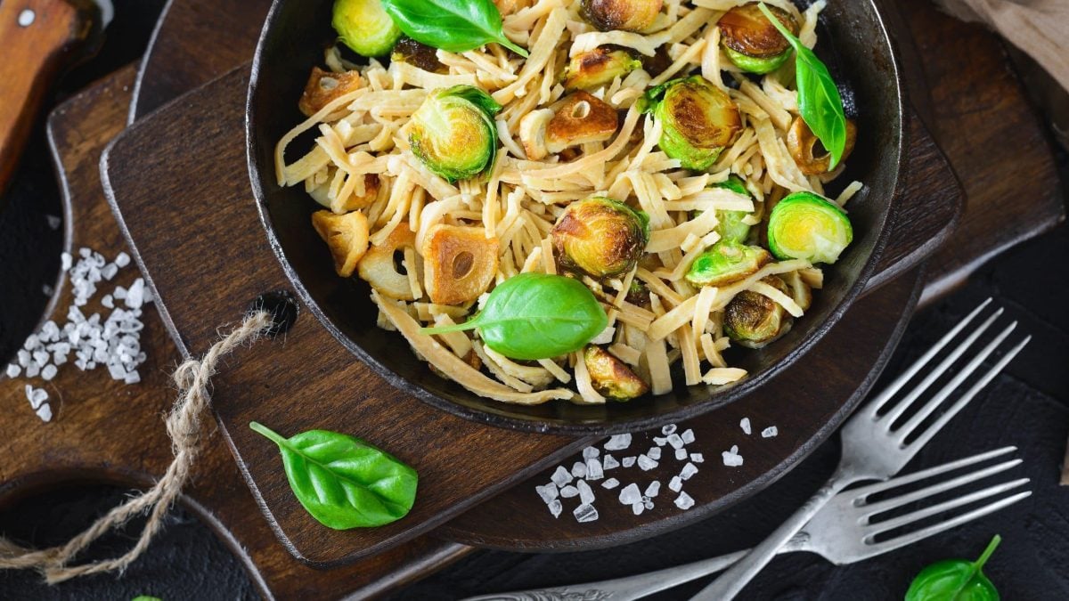 Draufsicht: Eine Rosenkohl-Pasta mit gebratenem Knoblauch. Drum herum liegen grobe Salzkörner und frische Basilikumblätter.