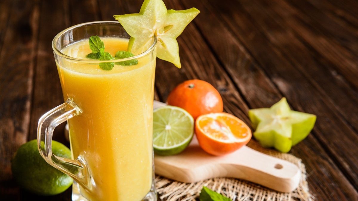 Frontal: Ein Sanddorn-Zitrus-Saft auf dunklem Untergrund. Drum herum liegen frische Zitrusfrüchte.
