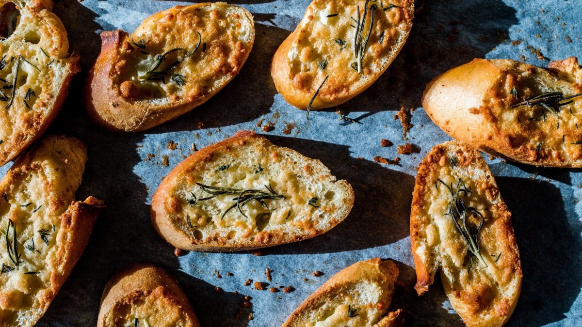 Draufsicht: Mehrere überbackene Käse-Knoblauch-Bruschetta auf blauem Untergrund.