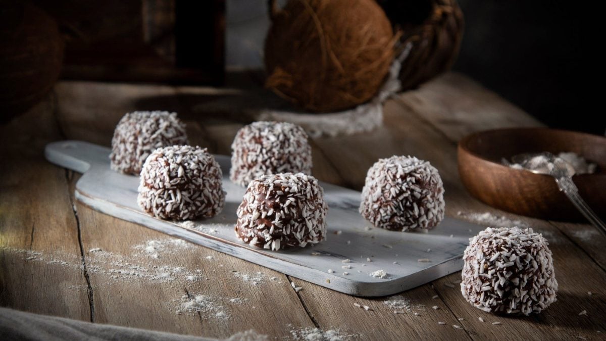 Dunkler Hintergrund: Auf einem rustikalen Holztisch liegen selbst gemachte selbst gemachte Weihnachts-Trüffel. die mit Kokosflocken bestreut sind.