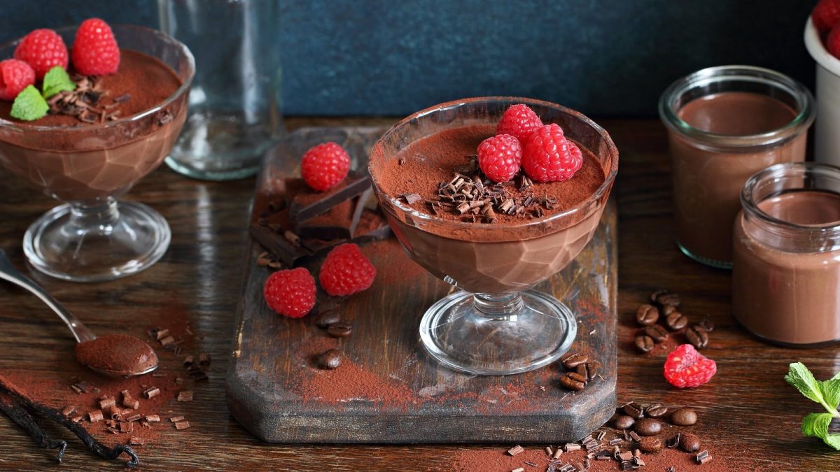 Ein Glas Schoko-Himbeer-Pudding auf einem Holzbrett.