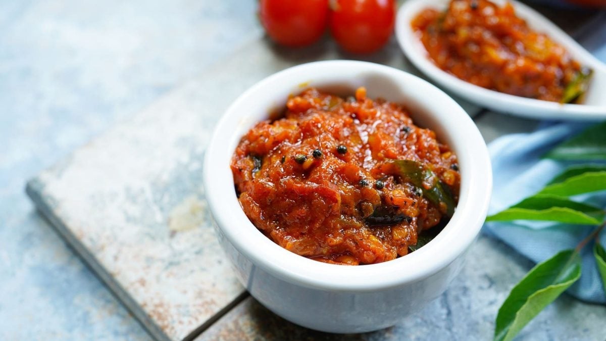 Eine kleine weiße Schüssel mit Tomaten-Chutney auf einem Marmorbrett.