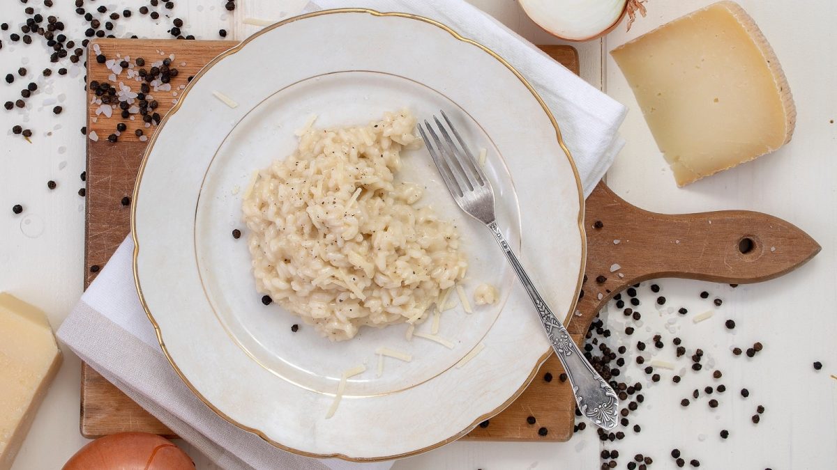 Ein weißer Teller mit Risotto Cacio e Pepe auf einem Holzbrett.