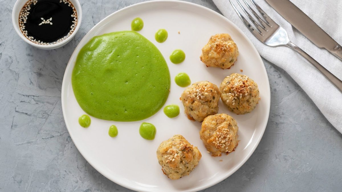 Ein weißer Teller mit Fischbällchen auf einem grauen Tisch.