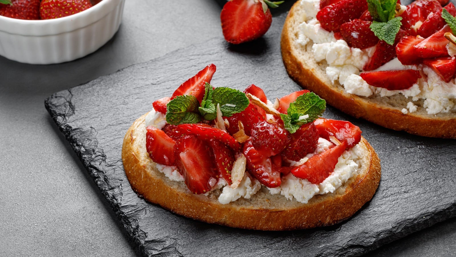 Ein Brot mit Cheesecake-Aufstrich und Erdbeeren auf einer Schieferplatte.