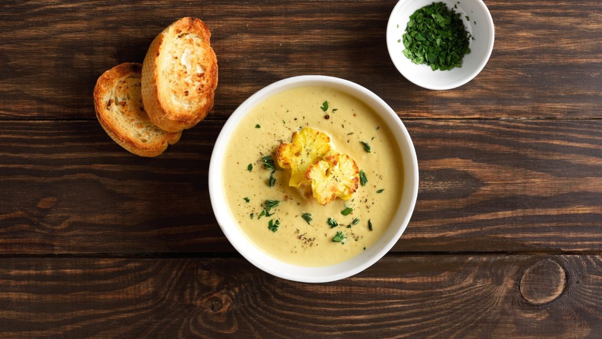 Eine Schüssel Blumenkohl-Curry-Suppe auf einem dunklen Holztisch.