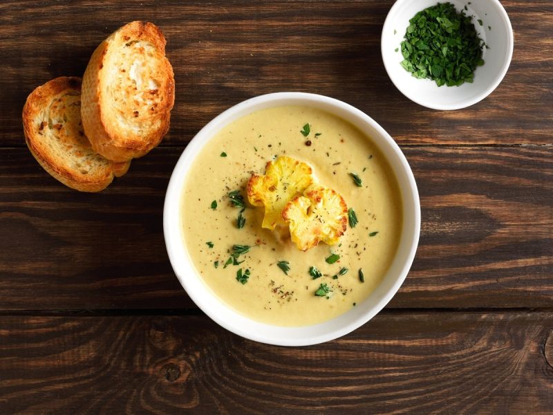 Eine Schüssel Blumenkohl-Curry-Suppe auf einem dunklen Holztisch.