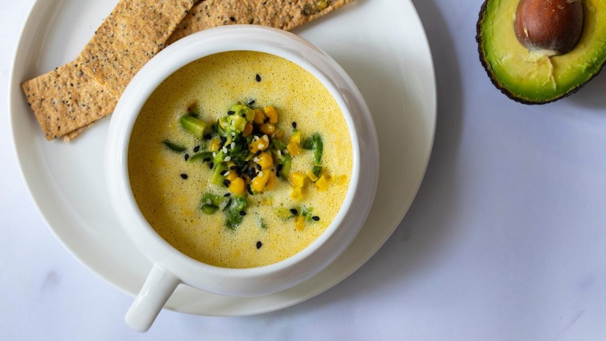 Die Avocado-Maissuppe in hellem Geschirr auf einem grauen Tisch direkt von oben fotografiert.