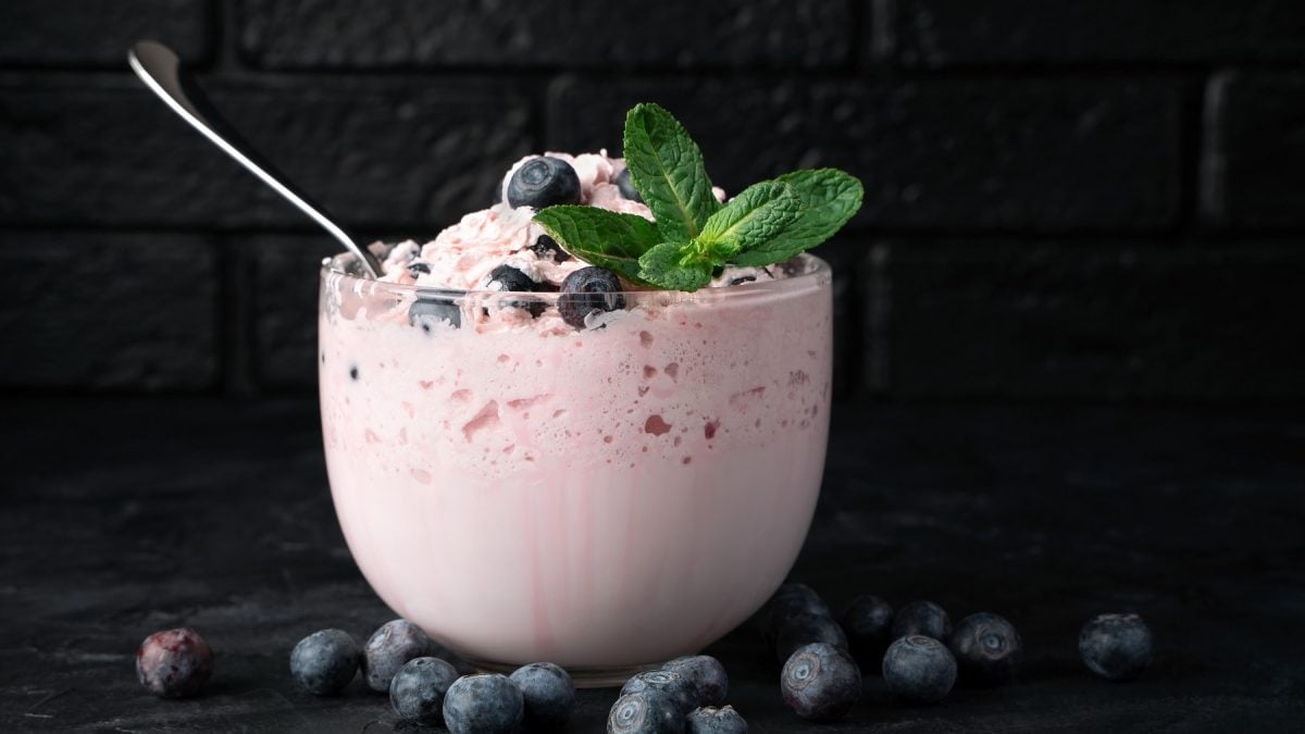 Ein Glas mit der Creme und Minze auf dunklem Untergrund mit Blaubeeren und schwarzem Hintergrund. Alles direkt von der Seite fotografiert.
