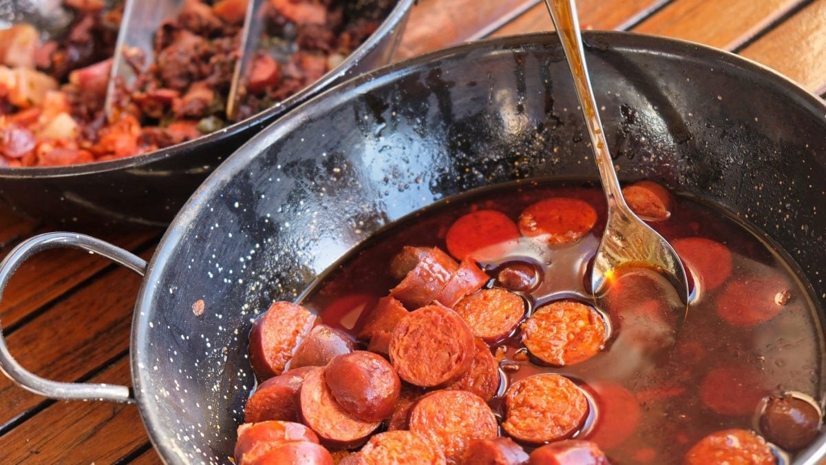 Draufsicht, schräg: ein weiter rustikaler Topf aus Metall mit Chorizos al vino.