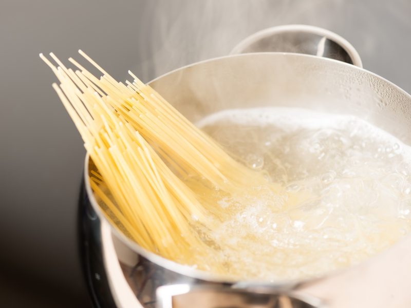 Draufsicht: Ein Topf aus Metall. In kochendem Wasser sind Spaghetti, die auch aus dem Wasser herausragen.
