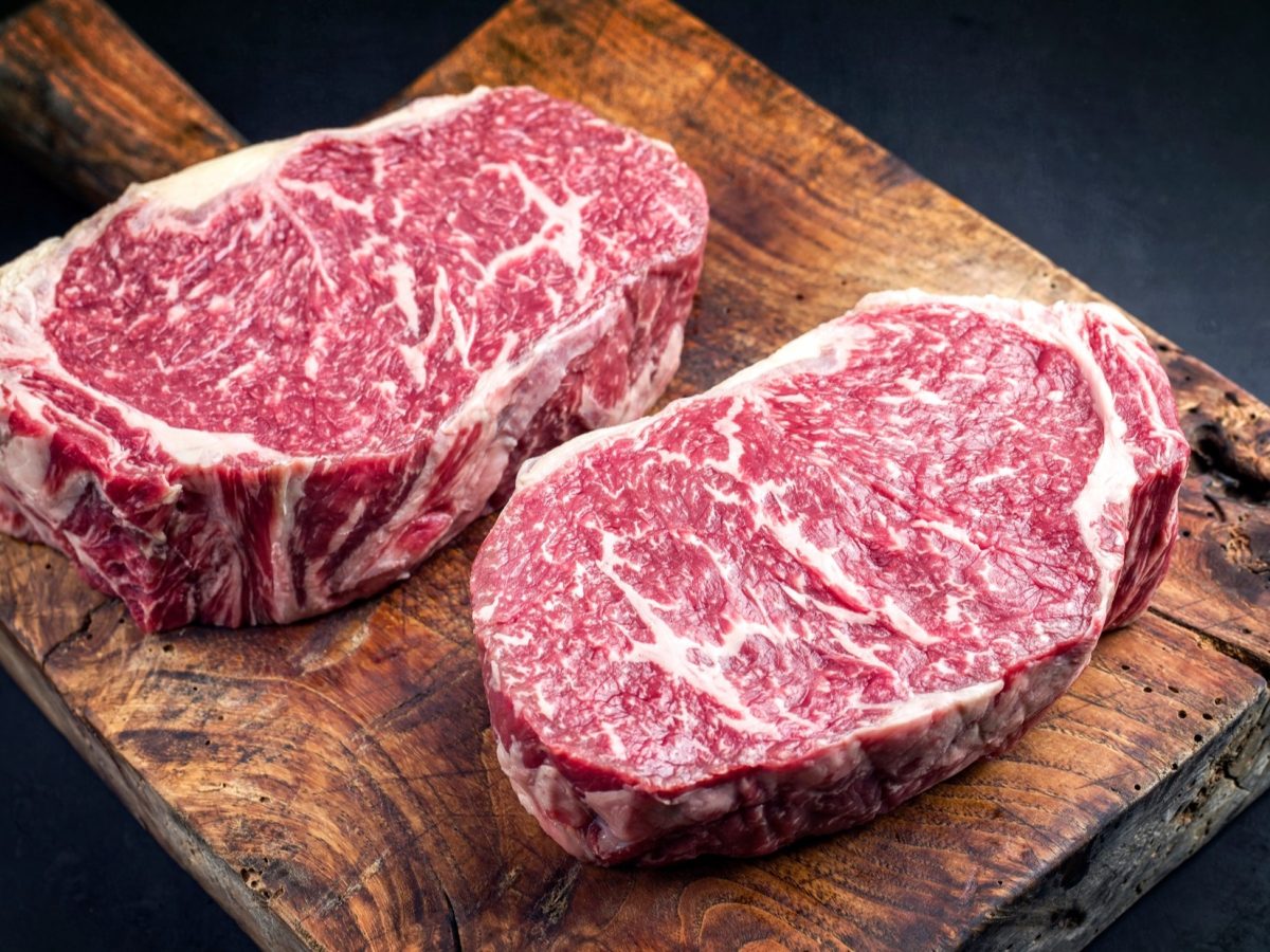 Draufsicht: Auf einem Holzbrett liegen zwei Steaks vom Wagyu-Rind.