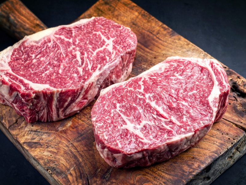 Draufsicht: Auf einem Holzbrett liegen zwei Steaks vom Wagyu-Rind.