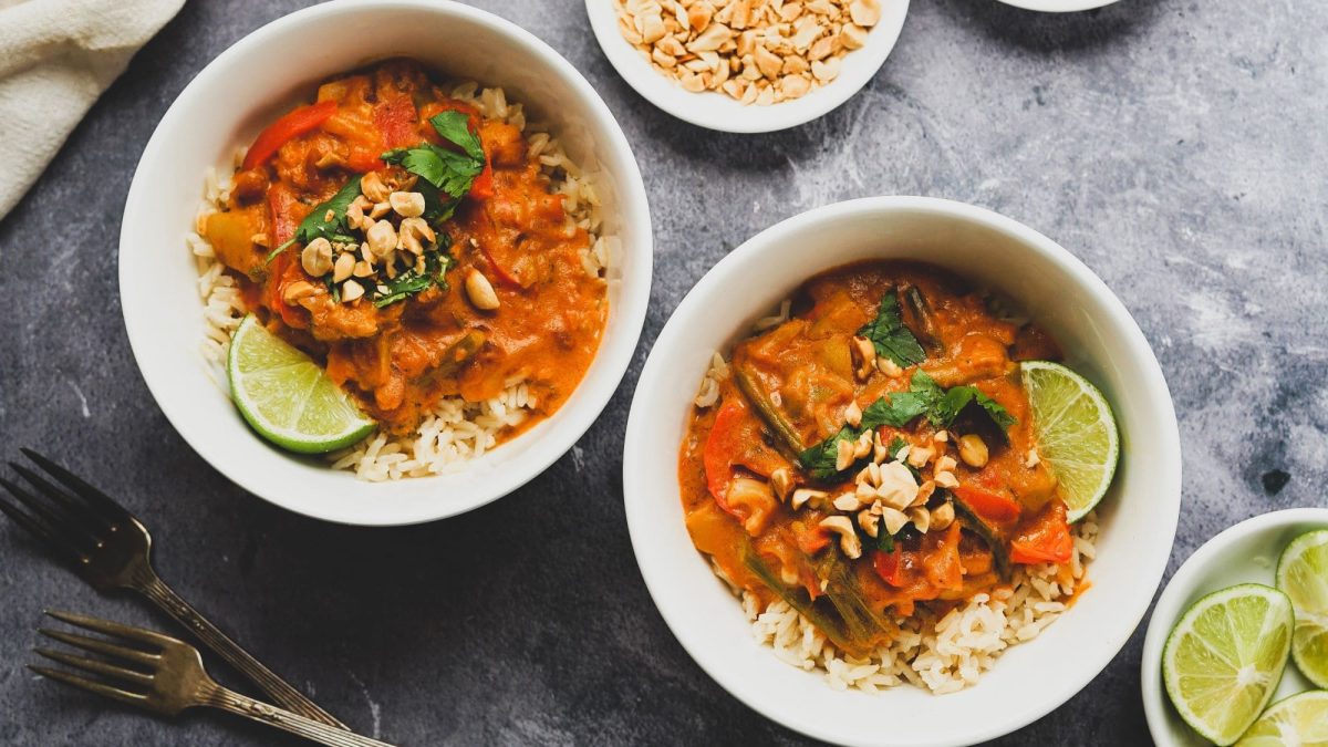 Zwei Schalen mit Erdnuss-Curry, garniert mit gehackten Erdnüssen und einer Limettenscheibe. Das Ganze ist angerichtet auf einem Tisch mit grauer, melierter Platte.